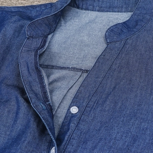 Détail de l'encolure en V et des boutons blancs sur une robe en jean bleu chambray