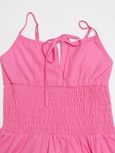Dettaglio di un abito estivo rosa con spalline sottili, fiocchi e corpetto elastico a punto smock
