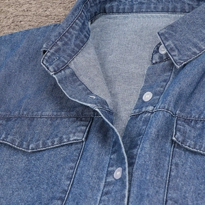 Dettaglio di un abito in denim blu con colletto classico e doppie tasche sul petto con bottoni