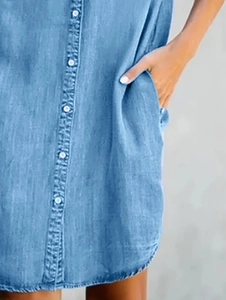 Detail of light blue denim shirt dress with white buttons and functional side pockets