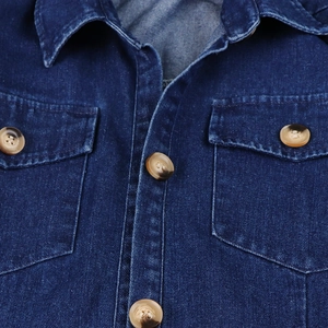 Detail view of denim shirt featuring lapel collar, chest pockets, and amber buttons
