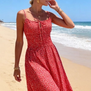 Abito lungo rosso a fiori con lacci e vita elasticizzata su una spiaggia soleggiata