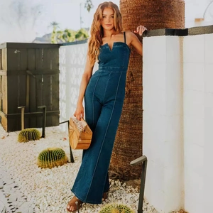 Slim fit dark blue denim jumpsuit with thin straps and wide leg pants in outdoor setting