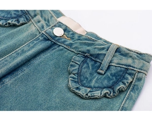 Détail de la taille en jean bleu clair avec poche à volants et bouton en métal argenté