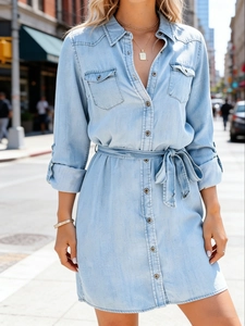 Detail of light blue denim shirt dress with metal buttons and waist tie belt