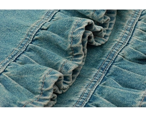 Détail macro du denim bleu clair délavé avec volants décoratifs et finition à double couture