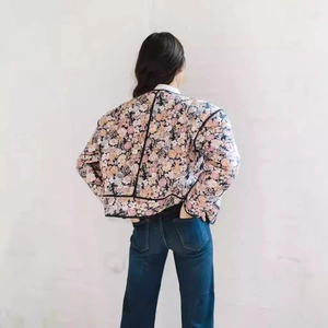 Detailed back view of a quilted floral cotton jacket with black piping and warm texture