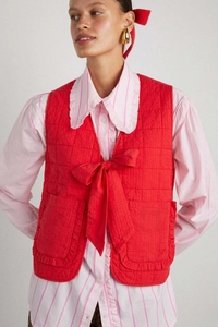 Detail view of red quilted vest featuring large bow ties and ruffled patch pockets