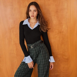 Detail of layered V-neck knitwear with blue striped shirt cuffs and green plaid pants