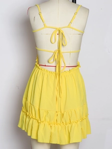 Detail of yellow backless dress featuring criss-cross lace-up straps and tiered ruffle skirt