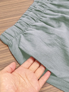 Detail of sage green elastic waist trousers showing deep side pockets and cotton texture