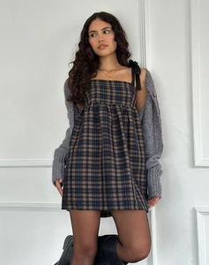 Détail de la robe courte à carreaux avec bretelles à nœuds et jupe plissée sous un gilet