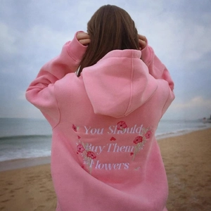 Detailed back view of pink oversize hoodie featuring floral embroidery and text on beach