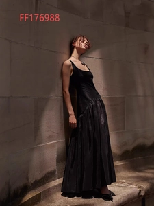Robe longue noire satinée sans manches avec jupe plissée devant un mur en pierre
