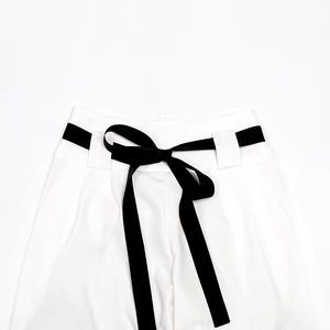 Detail of high-waist white wide-leg trousers with a black velvet bow ribbon belt
