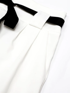 Detail view of white wide-leg trousers featuring a premium black satin ribbon bow tie