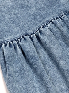 Close-up of acid wash denim dress featuring detailed stitching and pleated fabric texture