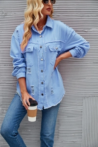 Close-up of light blue denim shirt with distressed ripped details and raw hem edges