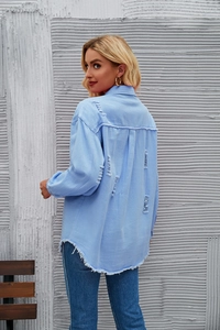 Detail of light blue denim shirt showing distressed ripped back and frayed hem style