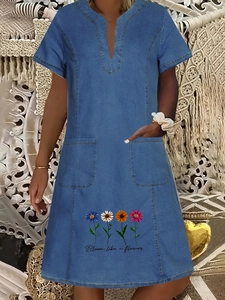 Detail of V-neck denim dress featuring large pockets and colorful daisy flower print