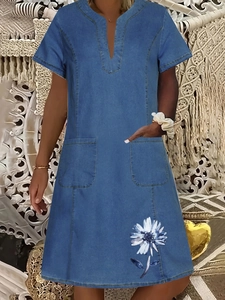 Detail view of denim dress featuring V-neckline and white daisy floral print on pocket