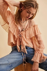 Close-up of ruffled V-neckline and tie detail on peach chiffon blouse with flared cuffs
