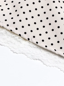 Close-up of pink polka dot fabric with intricate white floral lace trim detail