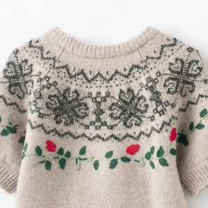 Close-up of beige knit sweater featuring geometric patterns and floral embroidery detail