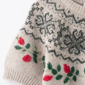 Detail view of beige knit sweater with black geometric patterns and red floral embroidery