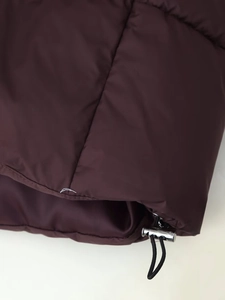 Detail view of the adjustable hem with metal toggle and elastic drawstring on burgundy puffer jacket
