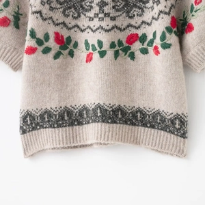 Close-up of floral embroidery and geometric jacquard on beige knitted short sleeve