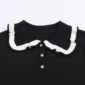 Detail of black ribbed knit shirt featuring white ruffle collar and crystal buttons