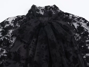 Detail of high neck lace dress with pussy-bow tie and floral embroidery patterns