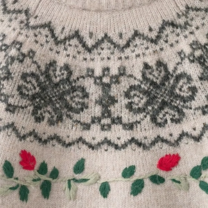 Detail of knit sweater neckline featuring red floral embroidery and jacquard patterns
