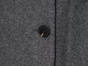 Detail shot of grey wool coat fabric with amber-patterned black button and thick texture