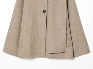 Detail of light camel wool coat showing texture, black button, and side pocket stitching