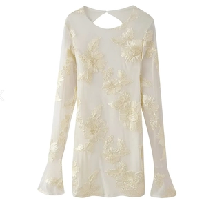 Détail macro de broderie florale crème sur robe en tulle à manches évasées élégante