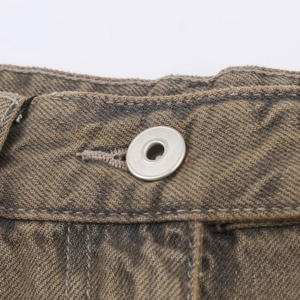 Detail of matte silver button and raw edge on brown vintage washed denim jeans