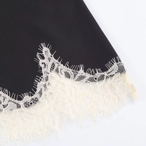 Detail of delicate white eyelash lace trim on the hem of a black satin camisole top