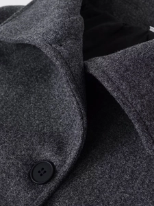 Gros plan détaillé sur la texture en laine gris foncé et le bouton noir de ce manteau chic