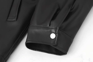 Close-up of black leather jacket cuff with silver metal snap button and fine stitching