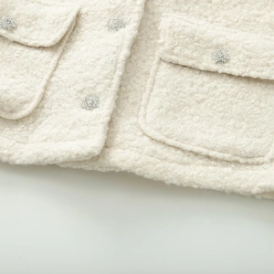Gros plan sur une veste crème texturée avec poches à rabat et boutons en strass brillants
