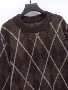 Detail showing the brown argyle knit sweater fabric texture and ribbed crew neckline