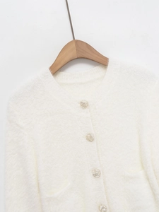 Detailed view of white fuzzy knit cardigan with silver wavy buttons and symmetrical pockets
