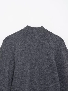 Flat lay of a dark grey knit sweater showing mock neck and raglan sleeve details