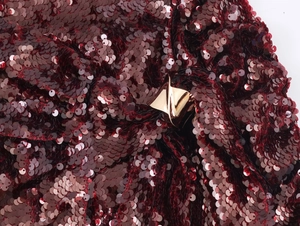 Macro view of sequined burgundy dress fabric with a twisted gold metal buckle detail