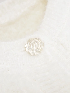 Macro detail of a silver wavy metal button on a white soft plush knit cardigan