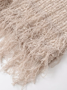 Detailed close-up of beige knitted fabric texture featuring elegant long fringe tassels