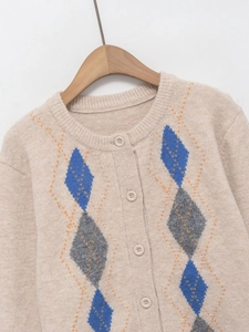 Detail of soft beige knit cardigan featuring blue and grey argyle pattern and round neck