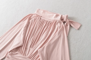 Detail of elegant apricot knit top featuring a high pleated neckline and side bow tie